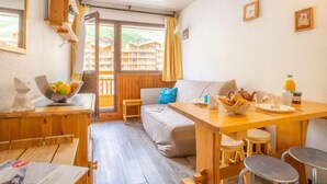 Une pièce chaleureuse avec une table en bois, un canapé et une fenêtre donnant sur des immeubles.
