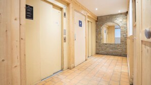 Un couloir aux murs en bois, un mur en pierre surmonté d’une arche, et un sol carrelé.
