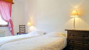 Camera da letto con due letti singoli, una cassettiera in legno, una sedia e due lampade da comodino.
