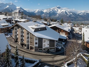 A snow-covered building with a prominent corner, a visible storefront, and a mountain backdrop. - Villars Soleil A27 by Interhome (Villars)
