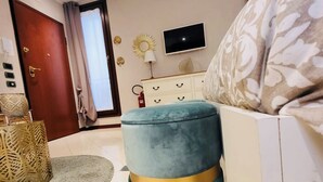 A modern bedroom with a teal ottoman, a white dresser, a flat-screen TV, and a patterned throw pillow. - A stone's throw from the Castle (Ferrara)