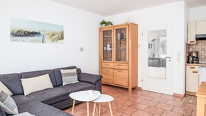 En stue med sofa, skab, lille bord og et tekøkken med kaffemaskine.