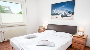 Et soveværelse med en seng, to sengeborde, et vindue, en radiator og et billede på væggen.