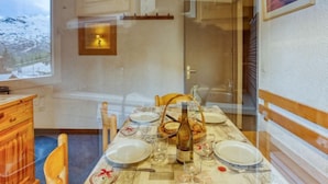 Uma sala de jantar com mesa posta para quatro pessoas, uma garrafa de vinho e vista para uma montanha nevada pela janela.