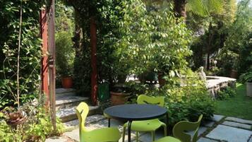 Un espace patio avec une table ronde et quatre chaises, entouré d’une végétation luxuriante et de plantes en pot.