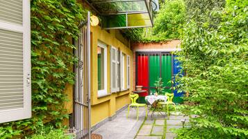 Une cour avec un mur jaune, un rideau rouge et vert, et une petite table entourée de chaises.