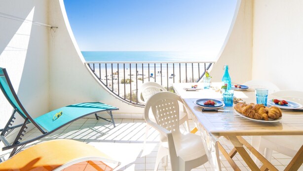 A balcony with a table set for breakfast, overlooking a beach. - Poséidon by Interhome (La Grande Motte)