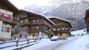 Une rue enneigée bordée de bâtiments en bois, de balcons, avec une chaîne de montagnes en arrière-plan.