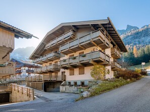 A multi-story building with balconies, a stone facade, and a mountainous backdrop. - Fontanelle by Interhome (Canazei)