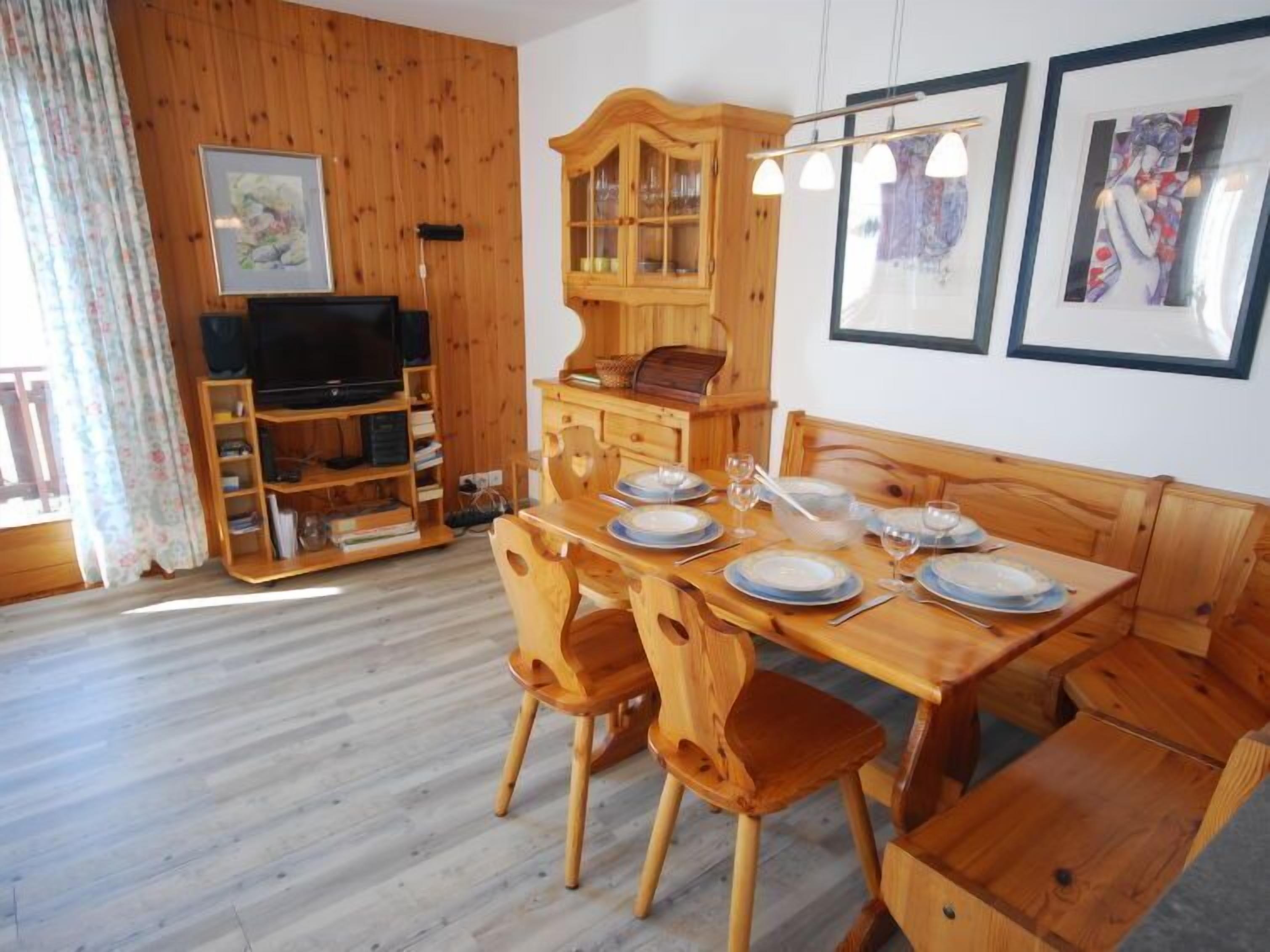 Un coin repas en bois avec une table dressée pour quatre personnes, un téléviseur dans un coin et un meuble avec des portes en verre.