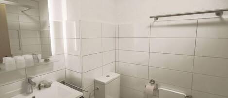 A modern bathroom with white tiles, a sink with a mirror, a toilet, and a shower area.