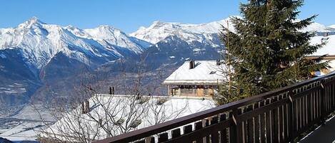 Une vue sur une montagne avec des sommets enneigés, un bâtiment en bois avec un toit recouvert de neige et une balustrade en bois.