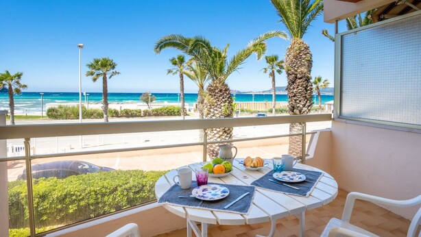 Een balkon met een tafel gedekt voor twee, met uitzicht op een strand met palmbomen en de zee.