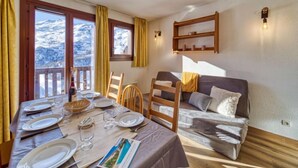 Una habitación acogedora con una mesa de comedor lista para cuatro personas, una litera y vistas a montañas nevadas a través de amplios ventanales.