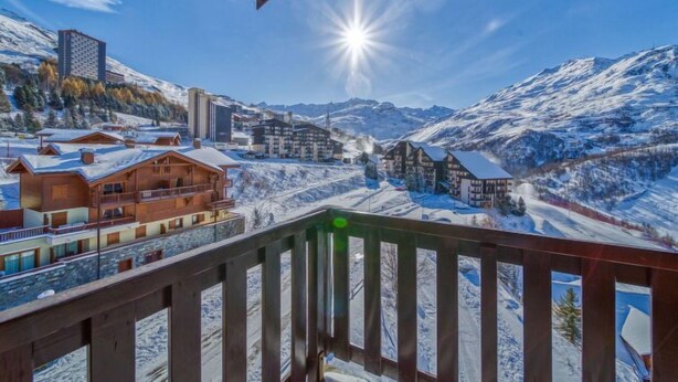 Un pueblo montañoso nevado con edificios de madera y una vista despejada del sol brillando sobre el paisaje.