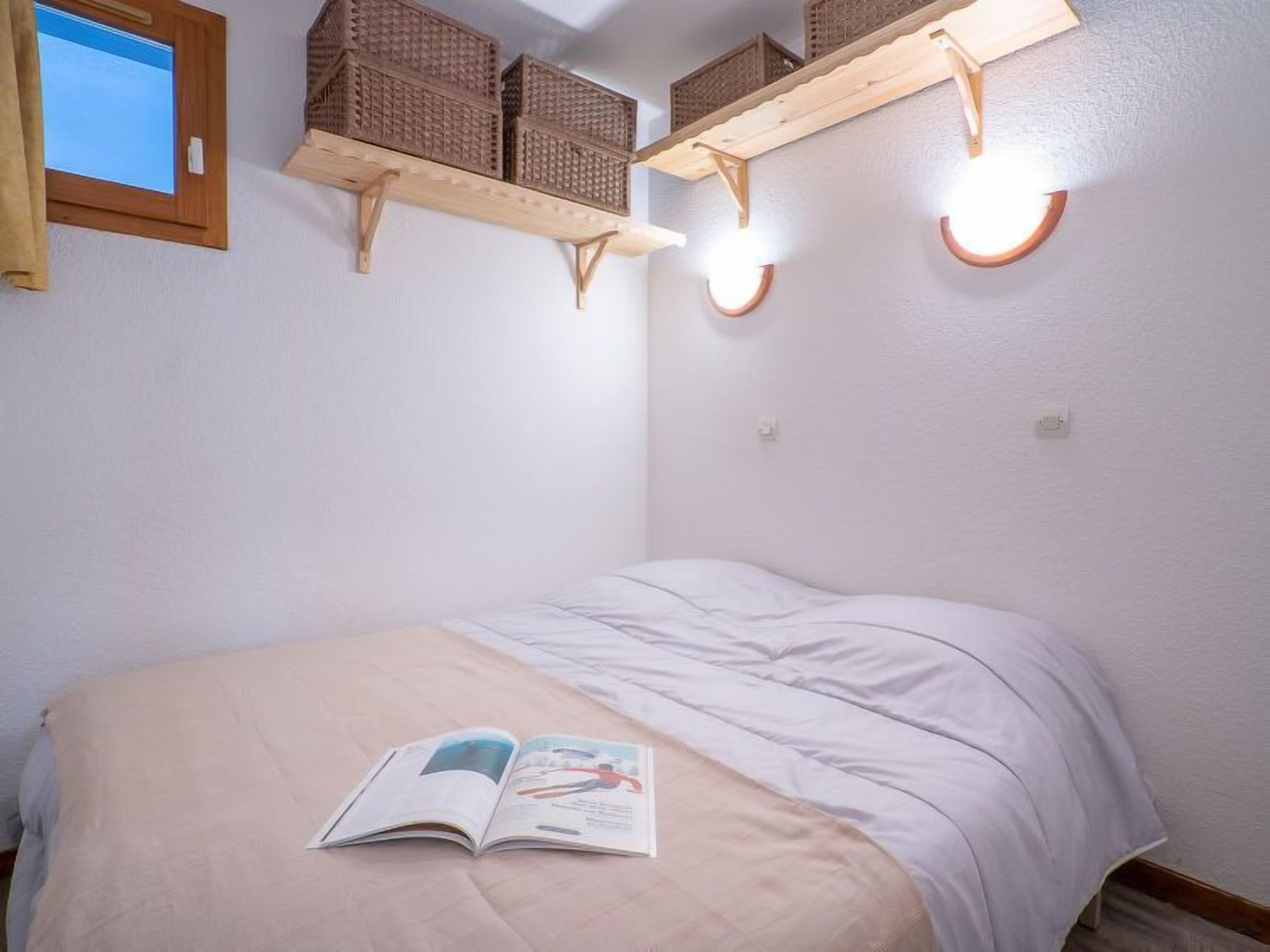 Une chambre à coucher avec un lit, une fenêtre et des étagères en bois avec des paniers.