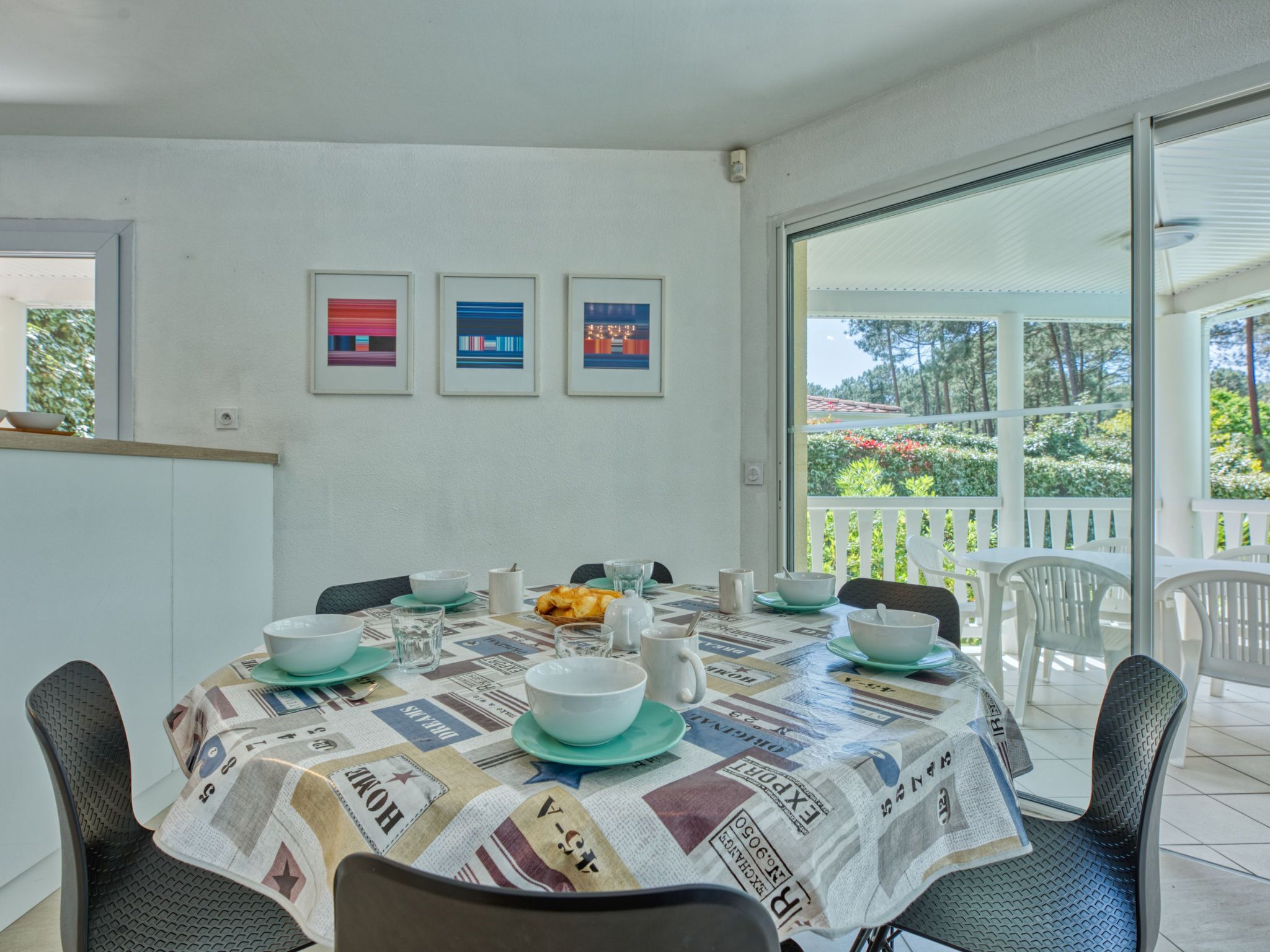A dining area with a table set for four, surrounded by chairs, with a view of greenery outside.