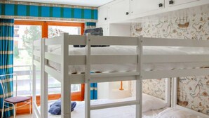 Dormitori amb literes, finestra, cortines i una cadira.