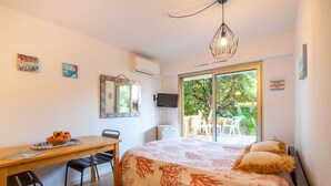 Une chambre avec un lit, un bureau et une chaise. Il y a un téléviseur accroché au mur, une fenêtre et une porte qui donne sur un balcon.