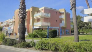 Un immeuble résidentiel à plusieurs étages, doté de balcons et entouré de palmiers et de verdure.