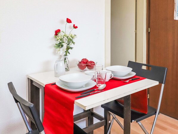 A dining table with white plates, bowls, and cutlery, a vase with red flowers, and a pitcher on the table.