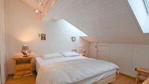 A bedroom with a large bed, two bedside tables, a skylight, and wooden flooring. - Apartment Apt 41 by Interhome (Canazei)