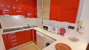 A modern kitchen with red cabinets, a microwave, a kettle, and a dishwasher. - Apartment Apt 41 by Interhome (Canazei)