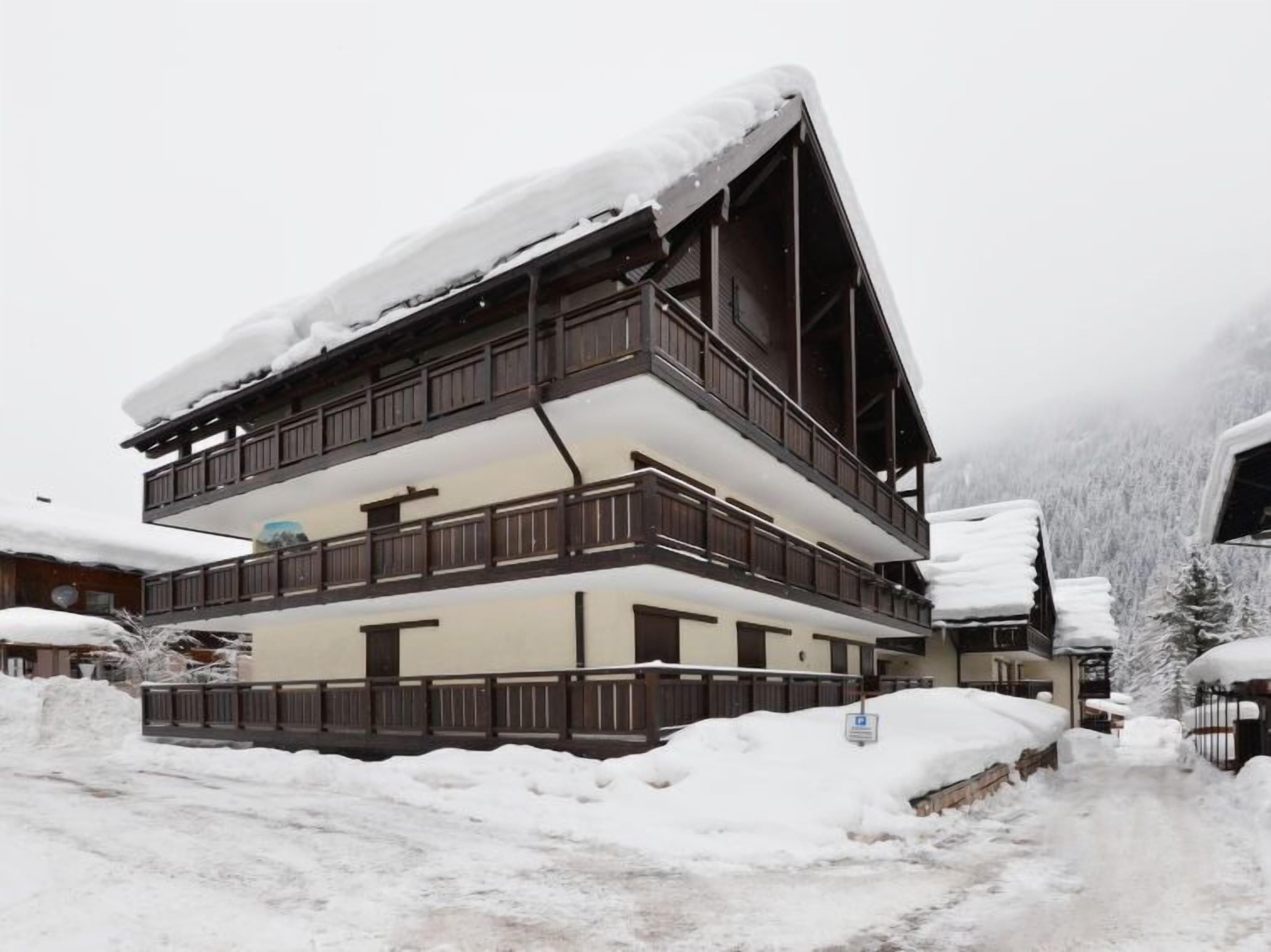 Un chalet à plusieurs étages doté de balcons, entouré d’arbres couverts de neige et surplombant un paysage montagneux.