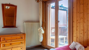 Una camera da letto con una cassettiera in legno, un termosifone e una porta scorrevole in vetro che dà su un balcone.