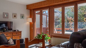 Una stanza accogliente con pareti in legno e ampie finestre, un tavolo da pranzo apparecchiato per due e una televisione su un mobile in legno.