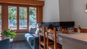 Un soggiorno accogliente con un divano, sedie di legno, un tavolo con bicchieri e una bottiglia, e vista attraverso ampie finestre.