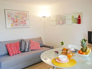 A living room with a grey sofa, colorful pillows, a round coffee table with breakfast items, and wall art.