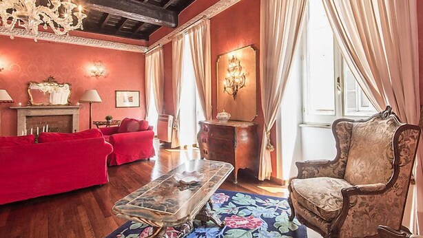 Une pièce avec un canapé rouge, une table basse en bois, un tapis à motifs, un lustre et une cheminée.