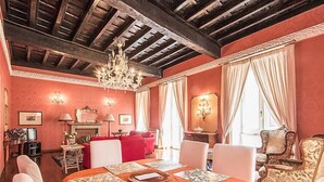 Un coin repas avec une table dressée pour six personnes, entourée de chaises, dans une pièce dont le plafond est orné de poutres en bois et qui est illuminée par un lustre.