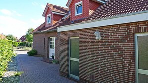 Une maison à deux étages, construite en briques, avec un toit recouvert de tuiles rouges, une porte d’entrée et une petite fenêtre.