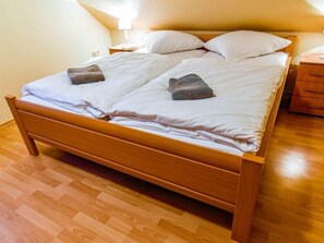A double bed with a wooden frame, white bedding, and two pillows. There is a nightstand with a lamp and a drawer unit to the right. - Tjalkstrasse by Interhome (Norddeich)