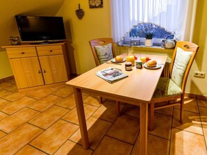 Ein gemütlicher Essbereich mit einem Holztisch, der für das Frühstück gedeckt ist, einem Fernseher auf einer Holzkommode und einem Fenster mit Blick auf einen Berg.