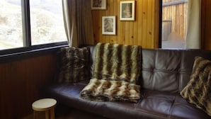 A cozy room with a leather sofa, a round wooden stool, and a large window with curtains. - Sérac A10 by Interhome (Val Thorens)