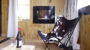 A room with wooden walls, a mounted TV, a black chair with a white and brown pattern, a table with a wine bottle and glasses, and a window with a view of buildings. - Sérac A10 by Interhome (Val Thorens)