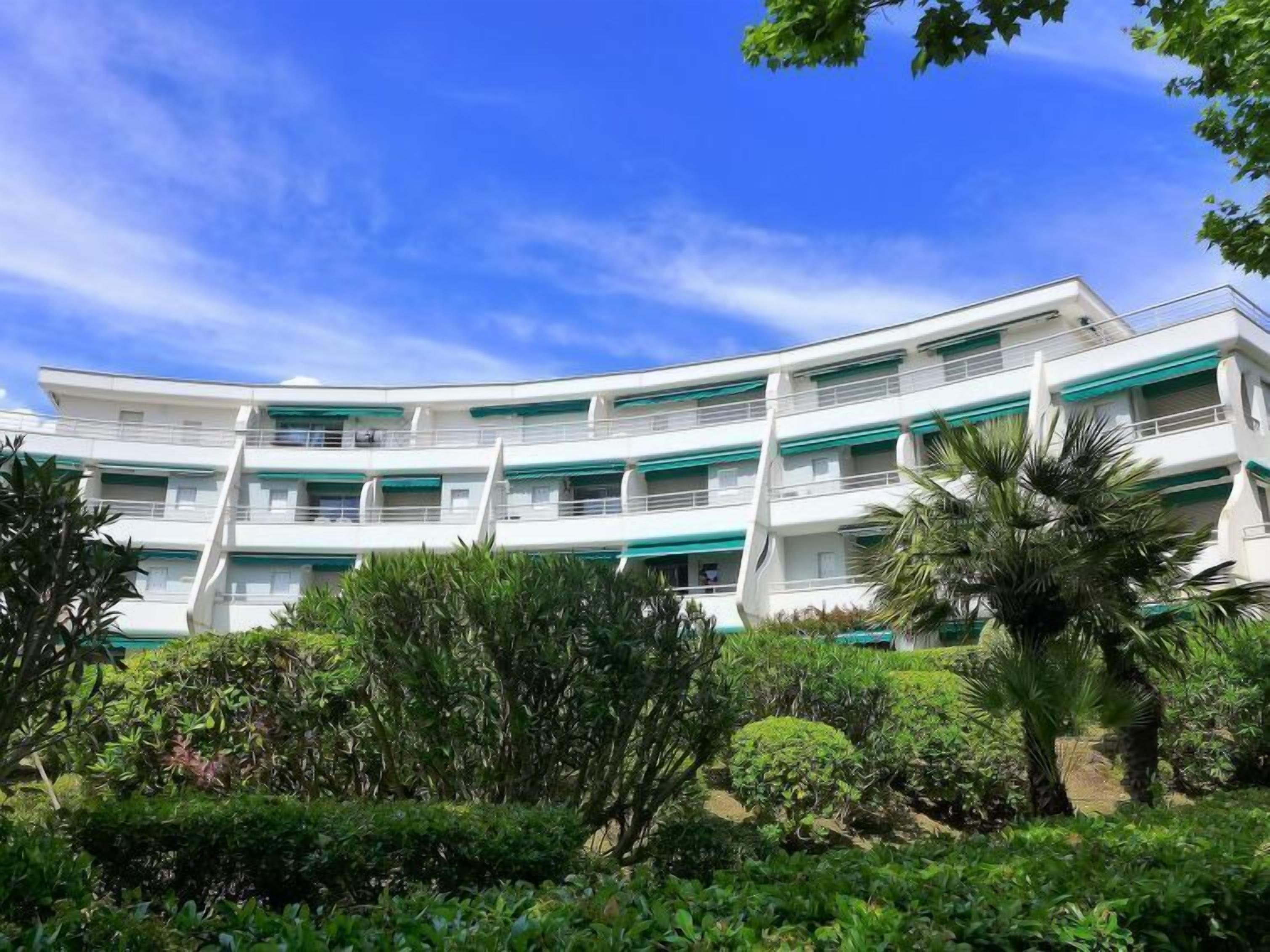 A multi-story hotel with balconies and a lush garden in front.