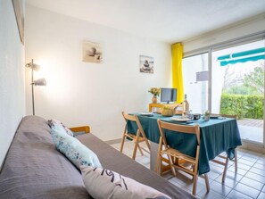 Una habitación acogedora con sofá, una mesa de comedor con sillas, televisor y ventana con cortinas.