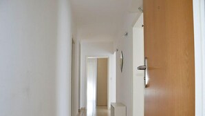 Un passadís amb una porta de fusta, parets blanques i un terra de rajoles.