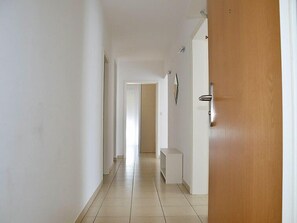 A hallway with a wooden door, white walls, and a tiled floor.