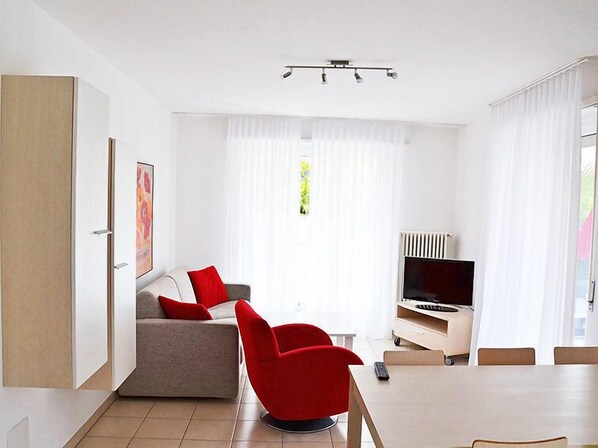 Un salon moderne avec un canapé, des fauteuils rouges, un téléviseur et une table à manger.