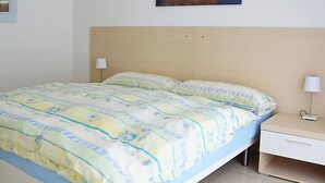 Un dormitori amb un llit, dues taules de nit, una petita taula i una làmpada penjada a la paret, i un quadre.