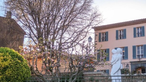 Un bâtiment à la façade rose, aux volets bleus, et orné d’une statue devant l’entrée.