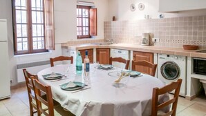 Une cuisine compacte avec un coin repas, un lave-linge et une fenêtre dotée de volets en bois.