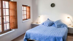 Une chambre à coucher avec un lit, deux fenêtres, une table de chevet et deux lampes de chevet.
