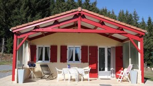 Um pequeno edifício térreo com telhado vermelho e paredes brancas, com um pátio com móveis de jardim e uma mesa.