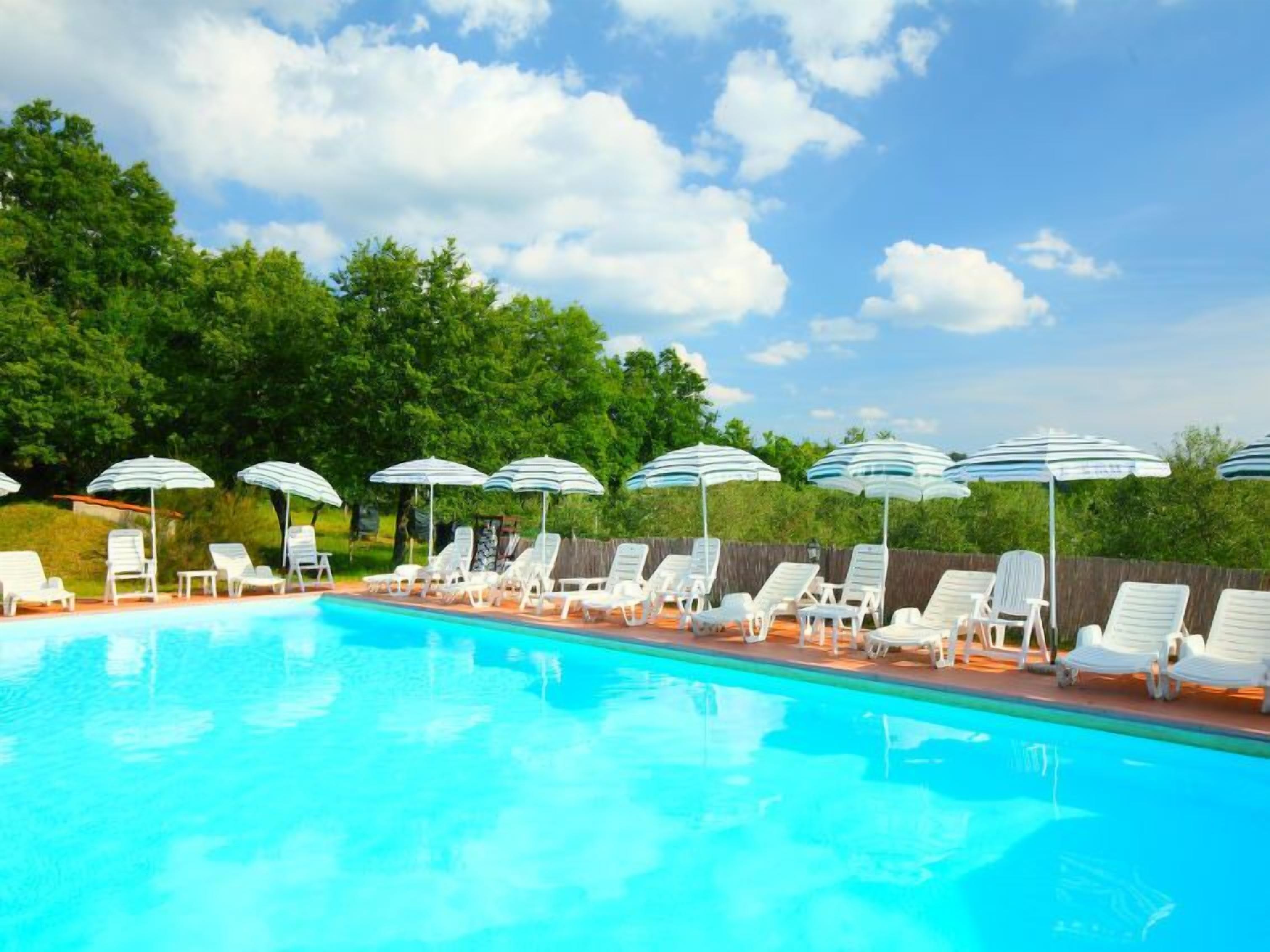 Una piscina con sillas reclinables blancas y sombrillas a rayas, rodeada de follaje.
